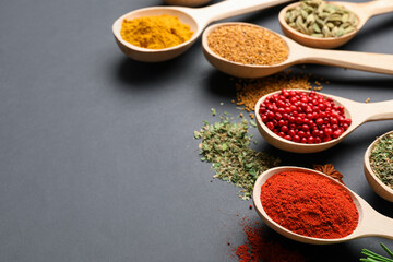 Different aromatic spices in spoons on black table, closeup. Space for text
