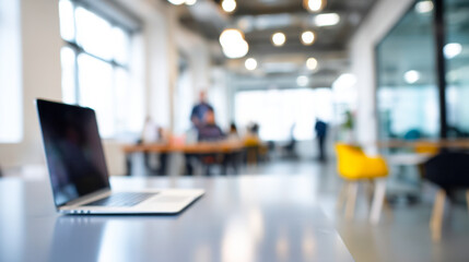 Fototapeta premium Modern office workspace featuring a laptop with blurred coworkers in the background