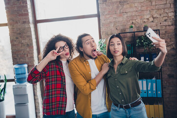 Young professionals taking a playful selfie together in a modern office environment depicting...