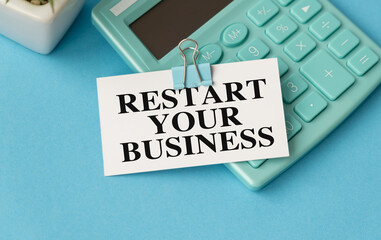 A calculator sits on a blue surface with a white sign that says Restart your Business