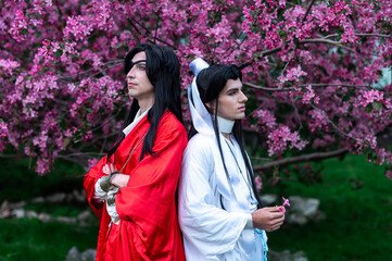 A male cosplayer with long hair in a kimono against a sakura background