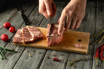 Hands skillfully cut through succulent meat portions on a wooden board. Fresh herbs and vegetables...