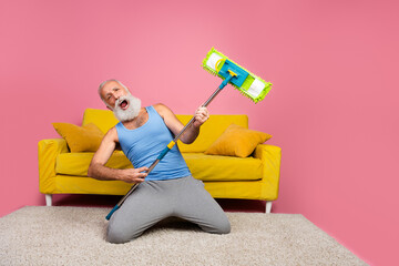 Elderly man enthusiastically pretending to play guitar on mop in colorful home interior