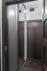 stylish corridor design in flat, apartment, hotel room or house. gray walls. wooden doors, beautiful chandeliers on ceiling. Soft lighting. furniture and entrance hall. large mirror in hallway