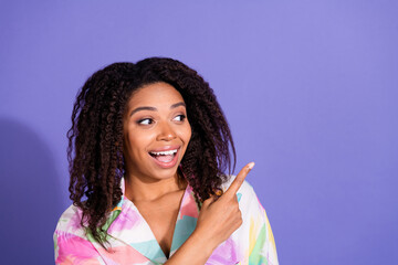 Young woman with a joyful expression points excitedly to the side against a vibrant purple...