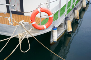Bright orange life buoy hanging on a boat's railing, surrounded by fenders and ropes, reflecting in...
