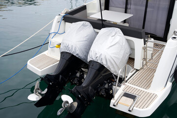 Twin outboard motors covered with protective fabric on a luxury yacht docked at a marina, showcasing modern boating technology and maintenance practices in a serene environment
