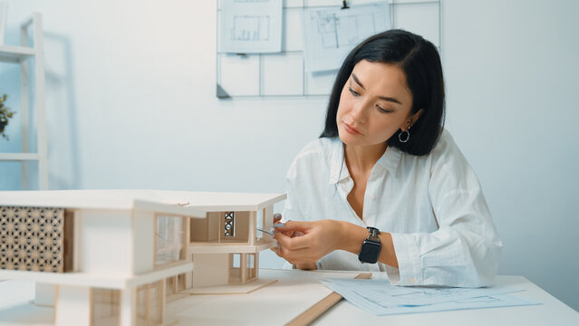 Closeup portrait image of professional young beautiful engineer architect using triangular scale measures house model with focusing at modern office. Business creative design concept. Immaculate.