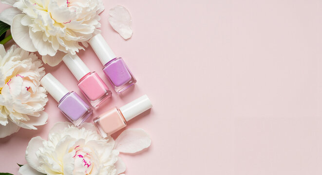 Nail polish bottles arranged with peonies on a soft pink background  