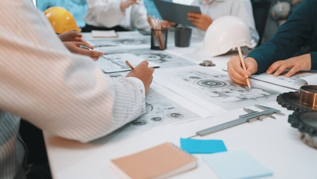 A dynamic scene of professionals collaborating in an engineering office. Team members engage in design discussions while analyzing sketches, tools, and project plans. SACTR