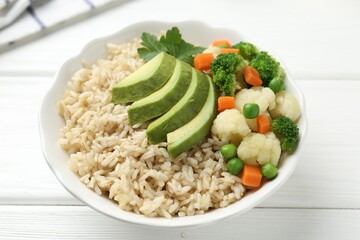 Tasty brown rice with vegetables in bowl on white wooden table, closeup