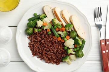 Tasty brown rice with vegetables and chicken served on white wooden table, flat lay