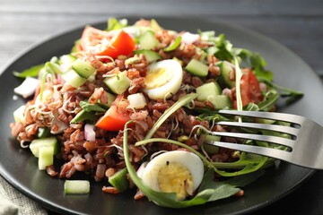 Delicious salad with brown rice on black wooden table, closeup