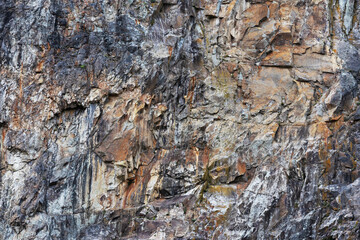 Part of a rocky wall photographed up close, highlighting its texture, formation, and colors.