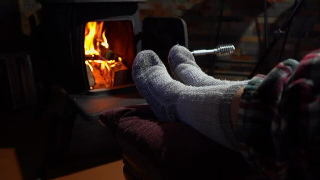 A woman warming her feet by a wood stove fire