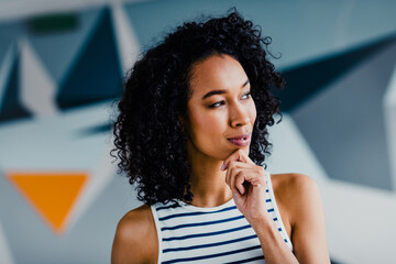 Confident young woman in casual striped top, indoors with geometric modern design, thinking creatively under natural daylight