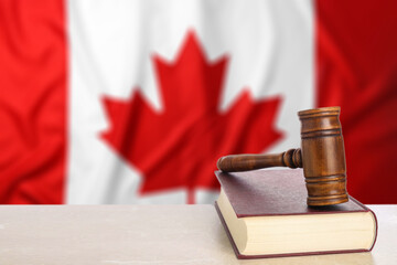 Judge's gavel and book on table against flag of Canada