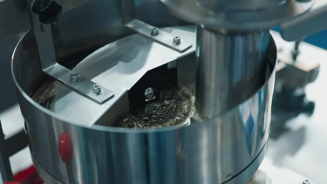 Close-up of a stainless steel grinding machine crushing dried herbal material in a clean laboratory setting.