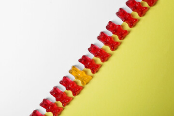 Individuality, uniqueness, different. Orange jelly bear among red ones on color background, top view
