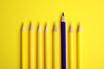 Individuality, uniqueness, different. Blue pencil among yellow ones on bright background, top view