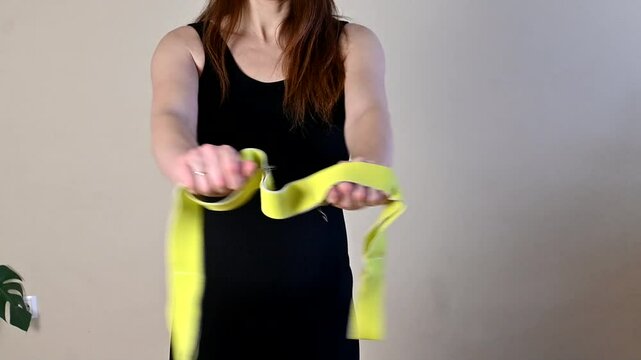 Pregnant girl in black sports suit doing fitness with elastic band, arm exercises