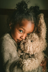 Dark-skinned girl embracing stuffed animal in cozy indoor setting  