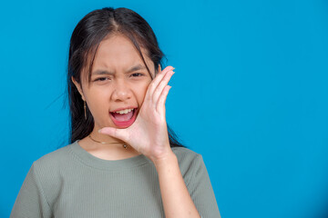 Portrait of a young Asian woman shouting with intense expression, hand cupped near mouth. Her bold,...