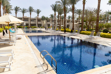 Summer seaside relax mood travel vacation a luxurious pool hotel interior for a summer holiday in warm countries. Beautiful tropical beach hotel resort with swimming pool, sun loungers palm trees