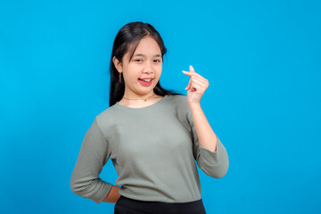 Charming young Asian girl smiling confidently while making a finger heart gesture with one hand....