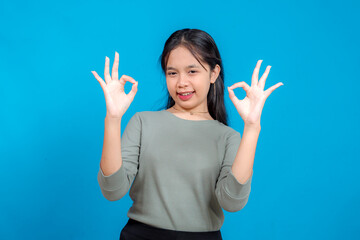 Smiling young Asian woman confidently showing double OK hand signs with a playful and cheerful...