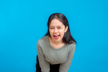 Obraz premium Young Asian woman with a wide, playful facial expression, squinting slightly and smiling with open mouth. Isolated on vibrant blue background. Concept of fun, energy, and confidence.