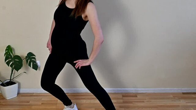 Pregnant girl doing fitness at home, standing half sideways and doing a leg lunge exercise