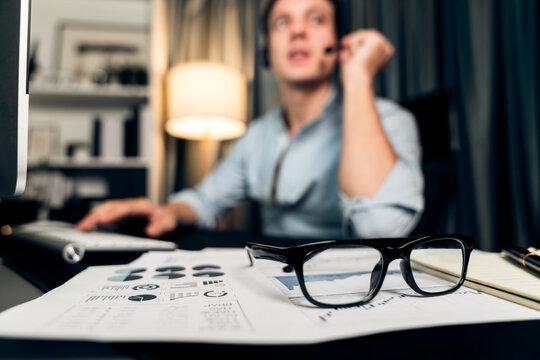 Call center consulting with customers on headphones on monitor in business paragraph with typing on pc with dynamic data marketing analysis planning at modern home office at night time. Pecuniary.