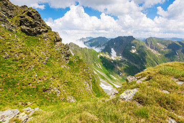 alpine landscape of romania in summer. vacation season. fagaras mountain ridge on a sunny day. scenic valley with snow on the grassy slope beneath a blue sky with clouds. travel to transylvania