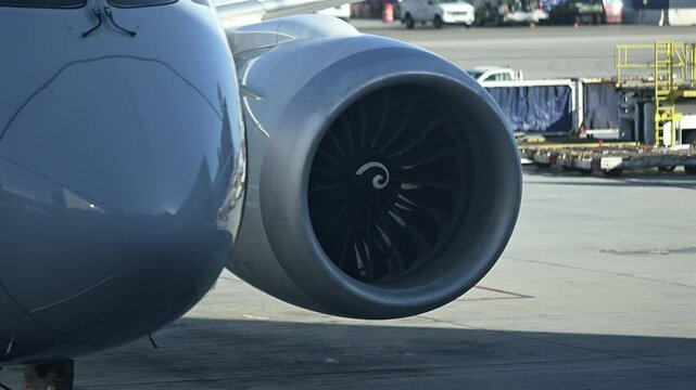 Close-Up View of Jet Engine Slowly Spinning on Parked Commercial Aircraft at Airport Gate with Ground Equipment in Background