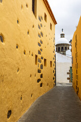 Narrow Historic Alley with Yellow Wall and Church Dome, A narrow cobblestone alley lined with a yellow historic wall leads to a domed church.