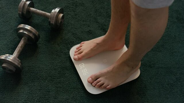 High angle shot of unrecognizable barefoot man stepping on white scale located on deep green rug