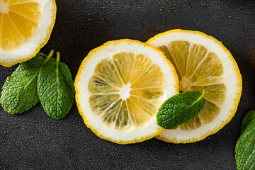 Fresh juicy lemon slices on a black background. Cocktail ingredient - mint leaves and lemon. Water...