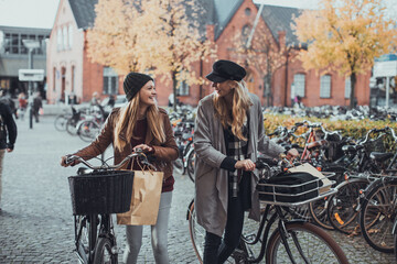 Obraz premium Young lesbian couple shopping and pushing their bicycles on a city street