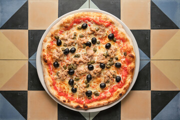 Delicious tuna pizza with capers and black olives on colorful tiles