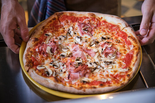 Chef placing delicious pizza with ham and mushrooms on metal counter