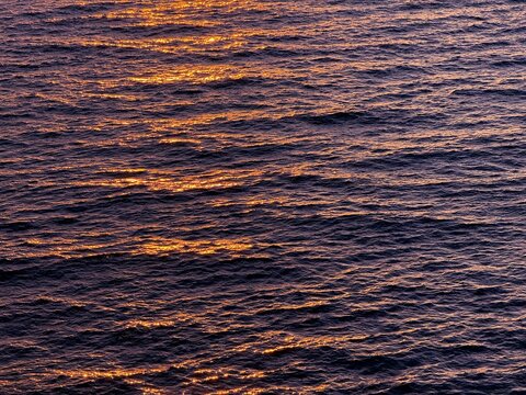 Evening sea waves surface with golden sun reflection.
