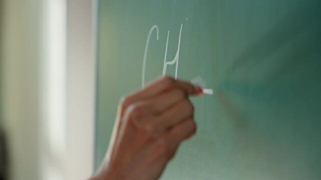 Close up female hand holding chalk writing math exercise on blackboard unrecognizable student girl woman teacher tutor studying learning write formula mathematic in university college school education