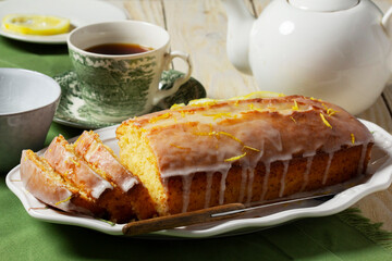 Aromatic lemon cake, covered with sugar icing and sprinkled with zest, served with tea.