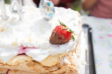 Close-up of a tempting meringue cake featuring whipped cream, a chocolate-dipped strawberry, and festive decoration. Perfect for celebrations and dessert visuals.