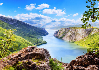Expansive view of the majestic Danube River winding through dramatic, forested cliffs and mountains. Captures a breathtaking panoramic natural landscape under a blue sky.