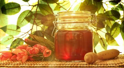 This image showcases a clear glass jar filled with golden honey, complimented by a wooden honey dipper and surrounded by vibrant flowers, set against a leafy backdrop. - obrazy, fototapety, plakaty