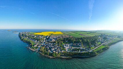 Aerial view of Ballycotton, a coastal village in County Cork, Ireland, with the ocean, lighthouse island, and yellow fields on a clear day.