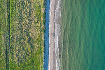 Top-down aerial view of a sandy beach meeting green dunes and turquoise sea in Ireland, with people casting long shadows in the evening light.