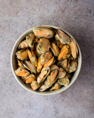 Cleaned boiled mussels in a bowl on a dark background, top view.